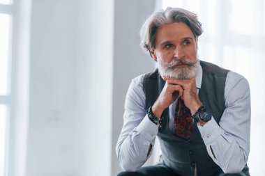 Ceketli ve kravatlı son sınıf öğrencisi pencereye karşı odada oturuyor..