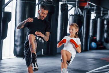 Temel yumruklar. Genç dövmeli boks koçu spor salonunda küçük tatlı bir kıza ders veriyor..
