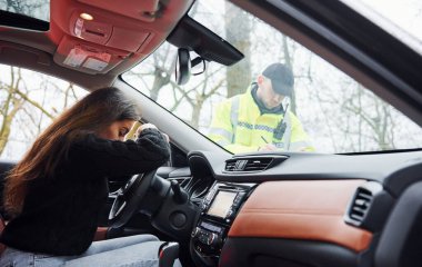 Kızlar kötü hisseder. Yeşil üniformalı erkek polis yolda aracı kontrol ediyor..