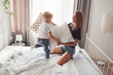 Anne, oğluyla gündüz yatak odasında yastık savaşı yapıyor..