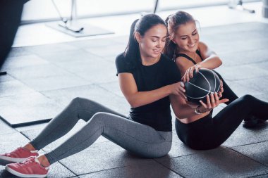 Spor elbiseli iki genç kız gündüz vakti spor salonunda toplarıyla yerde oturuyorlar..