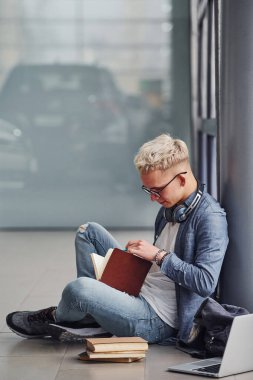 Genç hippi, gri arka planda oturuyor. Dizüstü bilgisayarı ve kitapları var..