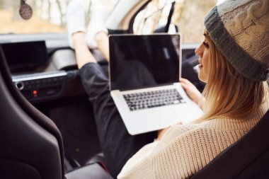 Laptop ve bir bardak içkiyle oturuyor. Kızın arabayla sonbahar gezisi var. Ormanda yepyeni bir otomobil..