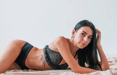 Siyah, mahrem iç çamaşırlı çekici esmer ve vücudunda dövmeleri olan kadın yerde yatıyor..