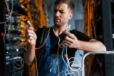 Üniformalı genç adam şaşkın hissediyor ve sunucu odasında internet teçhizatı ve kablolarla çözüm arıyor..
