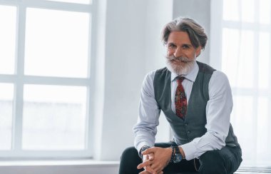 Ceketli, kravatlı, gülümseyen, pencereye yaslanmış bir adam..