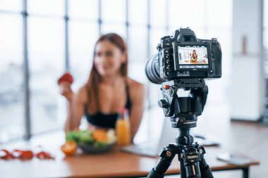 Spor vücutlu bir kadın vlogger 'ı. Sağlıklı yiyeceklerle birlikte evin içinde duruyor..