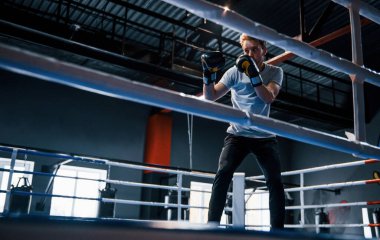 Beyaz gömlekli ve koruyucu eldivenli genç adam boks ringinde egzersiz yapıyor..