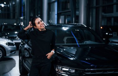 Esmer siyah otomobilin yanında duruyor ve gülümsüyor..