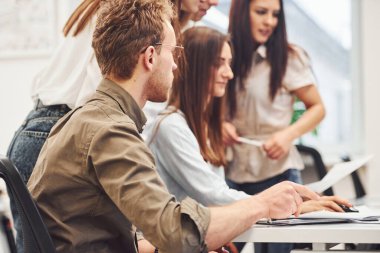 Genç iş adamları, modern ofiste masanın başında oturup konuşuyorlar ve birlikte çalışıyorlar..