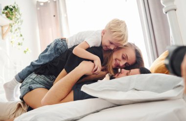 Genç evli çift ve küçük oğulları yatağa uzanıp gündüz vakti yatak odasında eğleniyorlar..