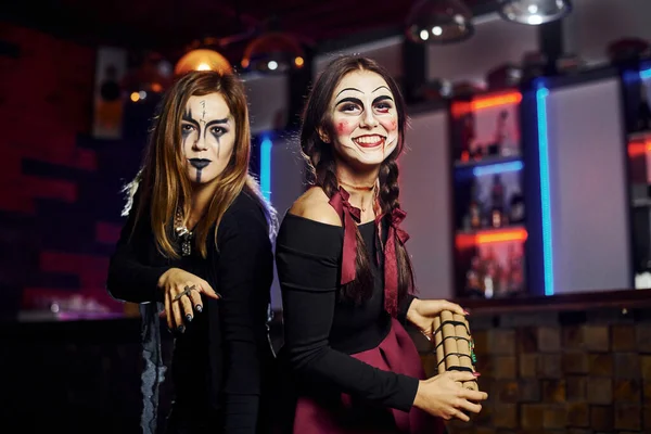 Two female friends is on the thematic halloween party in scary makeup and costumes with time bomb.