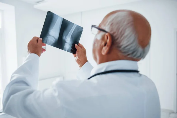 Hombre Mayor Médico Uniforme Blanco Examina Radiografía Piernas Humanas — Foto de Stock