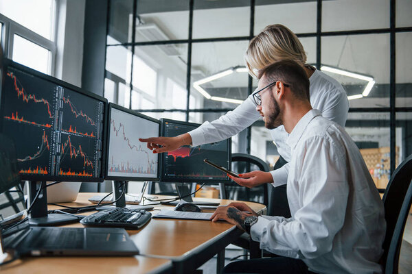 Analyzing information together. Two stockbrokers in formal clothes works in the office with financial market.