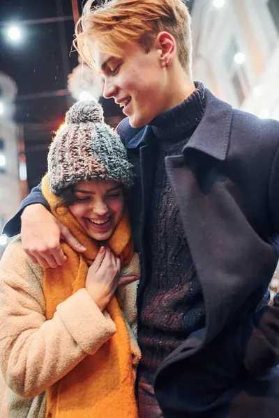 积极的年轻夫妇穿着温暖的衣服 在装饰过的圣诞大街上拥抱在一起 — 图库照片