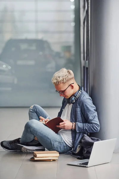 Genç Hippi Gri Arka Planda Oturuyor Dizüstü Bilgisayarı Kitapları Var — Stok fotoğraf