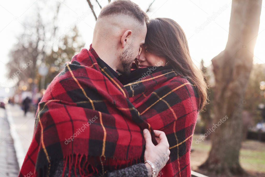 Warming by using red plaid. Happy multiracial couple together outdoors in the city. Asian girl with her caucasian boyfriend.