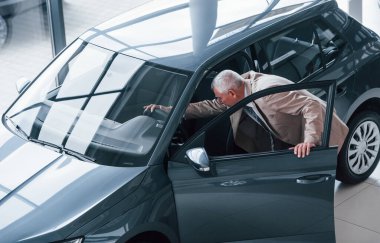 Resmi kıyafetli yaşlı bir adam araba kuaföründe yürüyor ve arabayı arıyor..