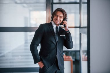 Ofisteki telefonun yanında konuşuyor. Siyah takım elbiseli ve kravatlı yakışıklı iş adamının portresi..