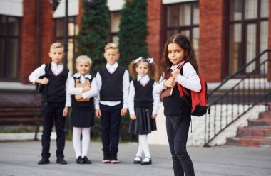 Okul üniformalı bir grup çocuk eğitim binasının yanında kameraya poz veriyor..