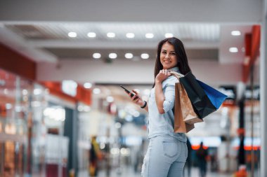 Süpermarkette elinde bir sürü paket ve telefonla esmer bir kadın alışveriş yapıyor..