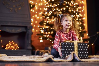Süslü Noel odasında hediye kutusuyla oturan tatlı küçük kız..