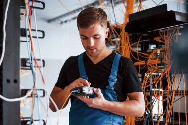 Ölçüm cihazlı üniformalı genç adam sunucu odasında internet ekipmanı ve kablolarla çalışıyor..