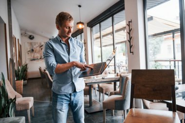 Gündüz vakti laptopuyla modern kafede olan adamın ön görüntüsü..