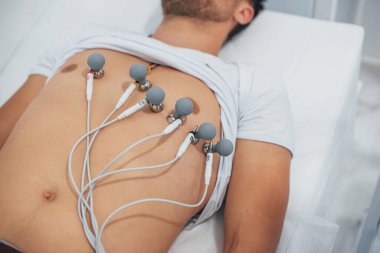 Klinikteki yatakta yatan ve elektrokardiyogram testi yaptıran bir adam..