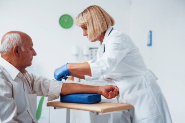 Kadın doktor klinikte yaşlı erkek hastaya iğne yapmaya hazırlanıyor..