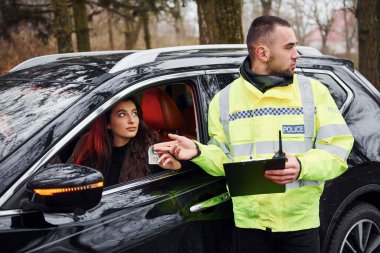 Yeşil üniformalı erkek polis memuru arabadaki kadından rüşvet alıyor..