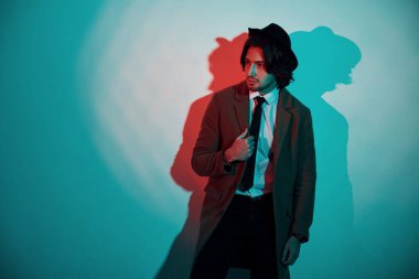 Şapkalı, takım elbiseli ve kravatlı genç bir adamın portresi stüdyodaki neon ışıklarda duruyor..