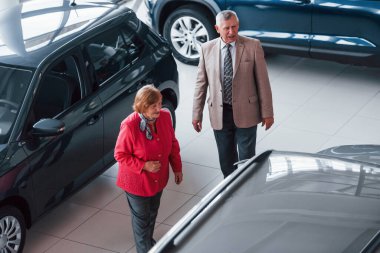 Resmi kıyafetli yaşlı adam otomobil seçiminde kadını destekliyor.