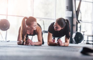 Spor elbiseli iki genç kız spor salonunda birlikte egzersiz yapıyorlar..