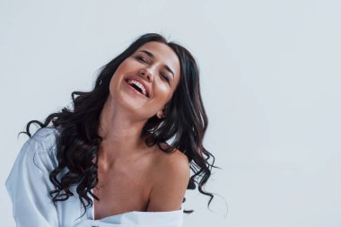 Beyaz ceketli genç esmer beyaz odada yatağın üzerinde oturuyor..