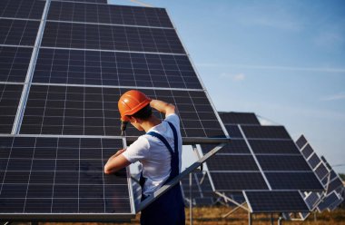 Kablosuz tornavida kullanıyor. Açık havada mavi üniformalı, güneşli bir günde güneş pilli bir erkek işçi..