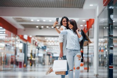 İki genç kadın süpermarkette alışveriş yapıyorlar ve selfie çekiyorlar..
