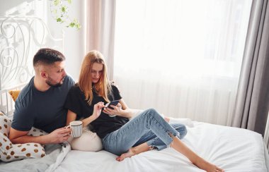 Telefon ve bir bardak içki. Genç evli çiftler gündüzleri yatak odasında vakit geçirirler..