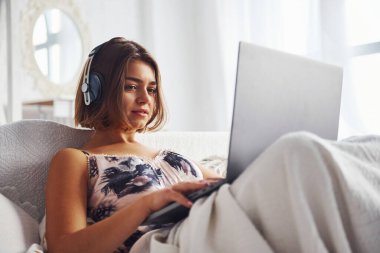 Kulaklık kullanarak müzik dinliyorsun. Hafta sonu vakti yatak odasında dizüstü bilgisayarla yatakta yatan tatlı bir kız..