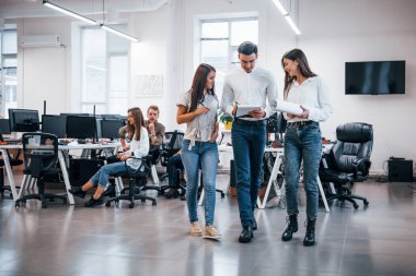 Bir grup genç iş adamı ofiste ayakta, oturarak ve çalışarak.