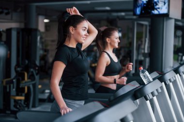Spor elbiseli iki genç kız koşu bandında spor salonunda beraberler..