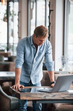 Gündüz vakti laptopuyla modern kafede olan adamın ön görüntüsü..