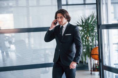 Ofisteki telefonun yanında konuşuyor. Siyah takım elbiseli ve kravatlı yakışıklı iş adamının portresi..