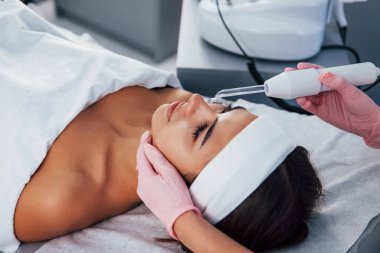 Kaplıca salonunda uzanan ve modern bir aletle yüz temizleme prosedürü uygulayan kadına yakından bakın..