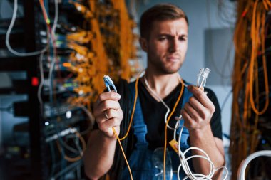 Üniformalı genç adam şaşkın hissediyor ve sunucu odasında internet teçhizatı ve kablolarla çözüm arıyor..