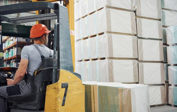 Üniformalı genç işçi depodaki forkliftte oturuyor..