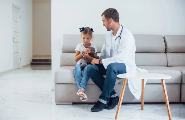 身穿白衣的男医生和小女孩坐在诊所里 — 图库照片