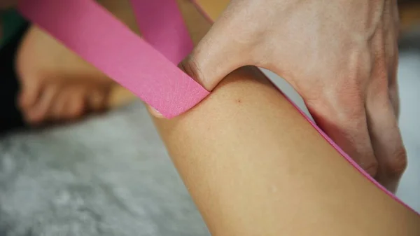 Doctor helps woman by leg treatment with kinesio tape.
