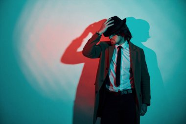 Şapkalı, takım elbiseli ve kravatlı genç bir adamın portresi stüdyodaki neon ışıklarda duruyor..