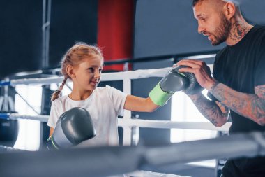 Boks ringinde birlikte antrenman yapmak. Genç dövmeli boks koçu spor salonunda küçük tatlı bir kıza ders veriyor..